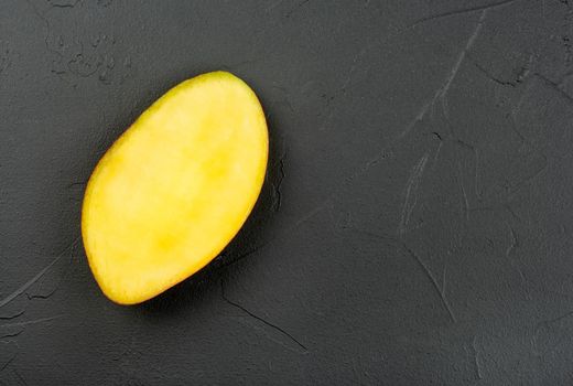 Juicy half of a ripe mango on a dark concrete background, top view