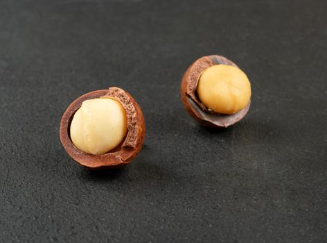 Two open macadamia nuts on a dark concrete background