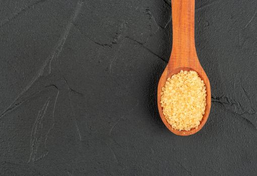 Brown sugar in a wooden spoon close-up on a dark background, top view