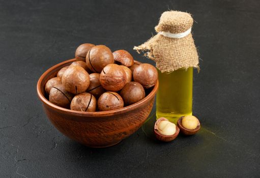 Oil bottle with a bowl of macadamia nuts on a dark background