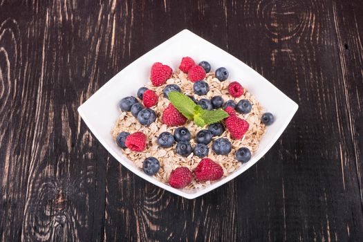White bowl full of oatmeal and raspberries and blueberries on a dark wooden background