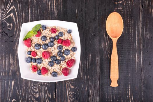 White bowl full of oatmeal and raspberries and blueberries and spoon on a wooden board