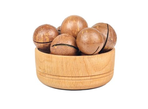 Macadamia nuts in a shell in a small wooden bowl on a white background