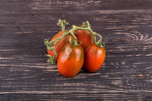 Sprig of red four tomatoes with drops on a dark wooden background