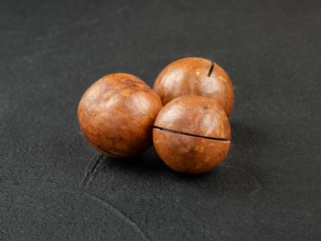 Three macadamia nuts on a dark concrete background