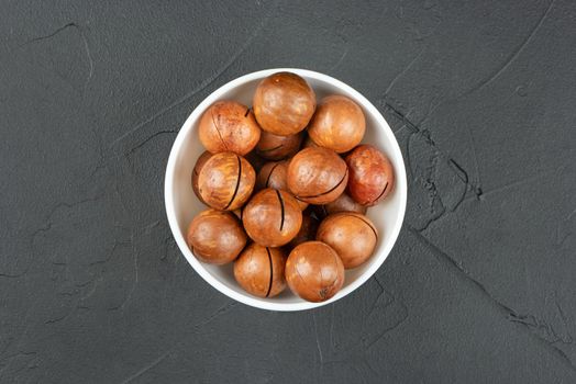 Macadamia nuts in a white bowl on a dark background, top view