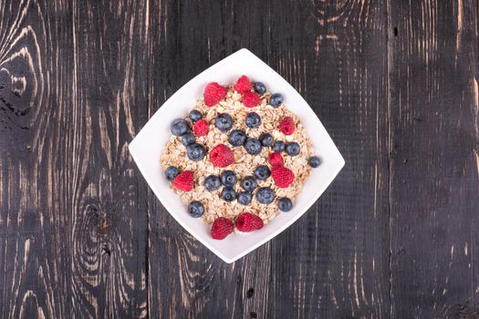 White bowl full of oatmeal and raspberries and blueberries and mint leaves on a dark wooden background