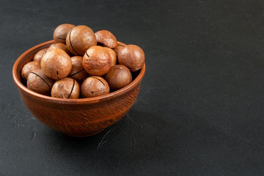 Macadamia nuts in a shell and bowl on a dark background