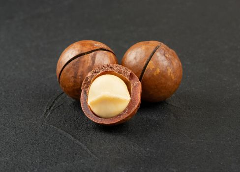 Three macadamia nuts on a dark concrete background