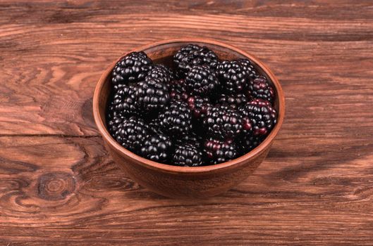 Plate full of fresh blackberries on a brown wooden table