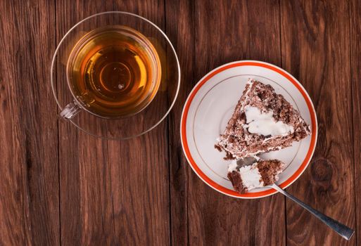 A cup of black tea with a piece of chocolate cake with cream on the table top view