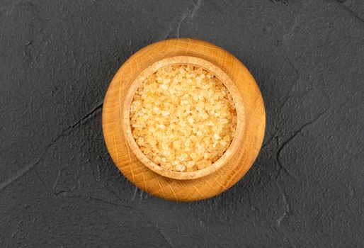 Wooden bowl with brown sugar on a dark background, top view
