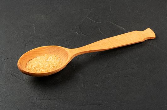 Large wooden spoon with brown sugar on a concrete background