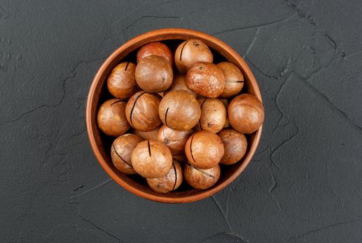 Macadamia nuts in a shell and bowl on a dark background, top view