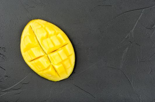 Juicy half of a ripe mango on a dark concrete background, top view