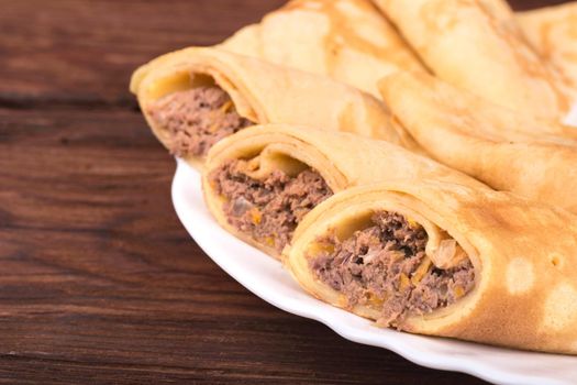 Three cut pancakes with meat on a plate on a brown wooden background