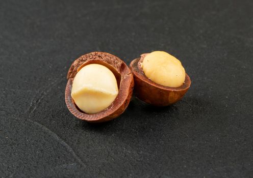Two open macadamia nuts on a dark concrete background