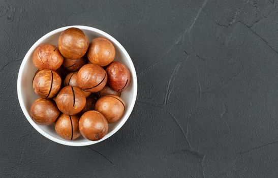 Macadamia nuts in a white bowl on an empty concrete dark background