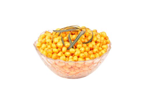 Glass bowl filled with fresh sea buckthorn berries with leaves on a white background