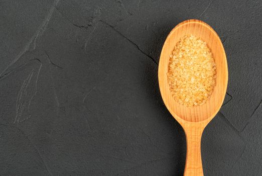 Large wooden spoon with brown sugar close up on empty dark background