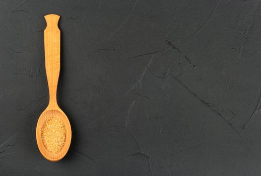 Large wooden spoon with brown sugar on an empty dark background