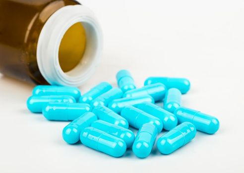 Scattered blue capsules from a bottle on a white background