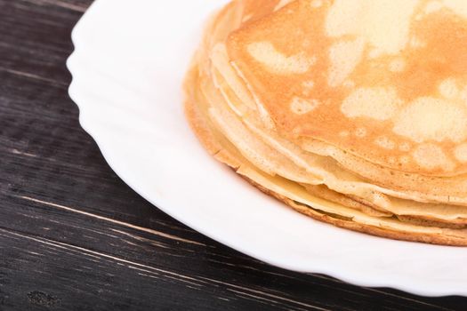 A pile of fresh pancakes on a white plate on a dark wooden table
