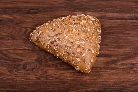 Triangular bun with different grains on a brown wooden background