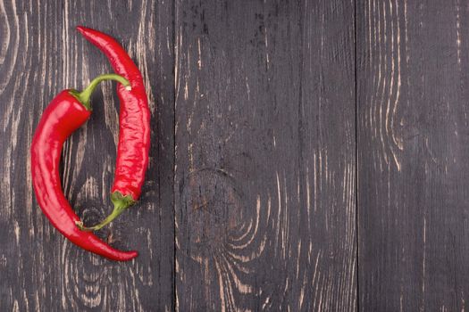 Two fresh red hot chili peppers on a dark wooden background under a text or a recipe