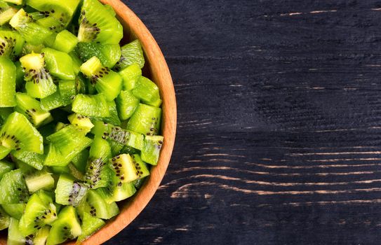 Half full bowl with a salad of kiwi on a wooden background top view