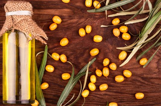 Bottle of sea buckthorn oil with berries and leaves on wooden background top view