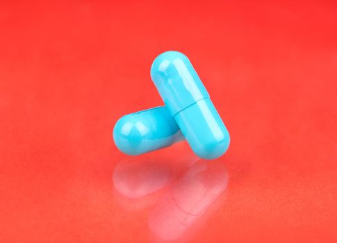 Two blue capsules are stacked on each other on a peach background