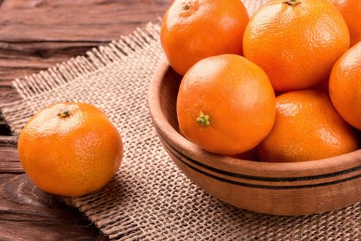 Wooden bowl filled with fruit mandarins on a napkin sackcloth closeup