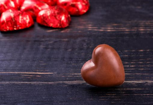 Several chocolate candies in foil and shape of the heart on a dark wooden table