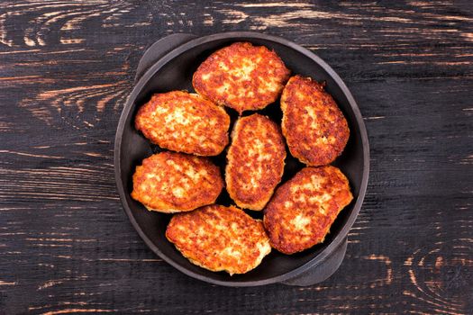 Fried cutlets in a cast iron skillet on a dark wooden background