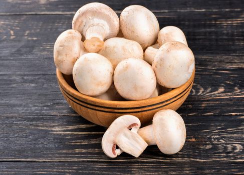 Raw champignon mushrooms in a bowl on a wooden background
