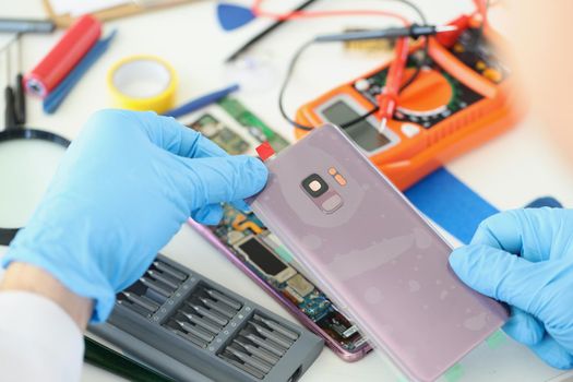 Technician repairs broken smartphone at table in workshop. Repair and diagnostic gadgets concept