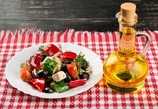 Plate with fresh Greek salad and bottle of oil on the table