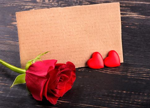 Blank paper valentine card with two hearts and a red rose on a wooden background