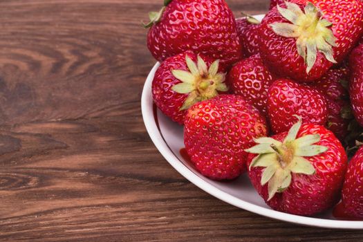 Bowl full of ripe fresh strawberries on a wooden background closeup