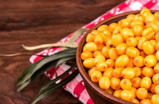 Part a bowl of sea-buckthorn berries on the tablecloth, and on the wooden background