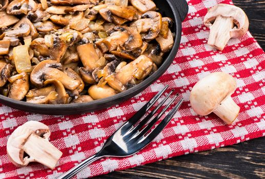 Part of the frying pan with fried mushrooms champignon and fork on a towel