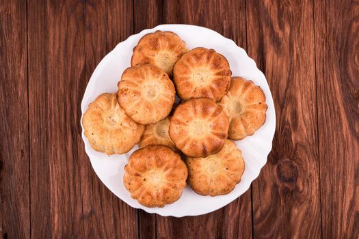 Homemade fresh baked biscuits on a white plate on a brown wooden background top view