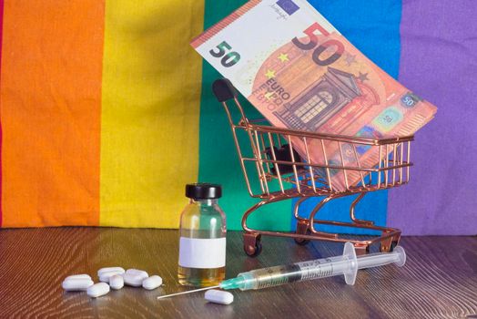 Injection, vaccine vial and medicinal tablets, Euro banknotes in a shopping cart on a background of a pride rainbow flag.