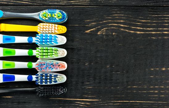 Multicolored toothbrushes on a blank wooden background, top view