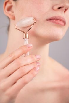 Close-up portrait of a woman using a quartz roller massager on her cheek for an alternative anti-aging