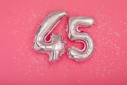 Silver balloon number 45 fourty five shape sparkles scattered randomly on juicy pink background. Silver confetti pink background