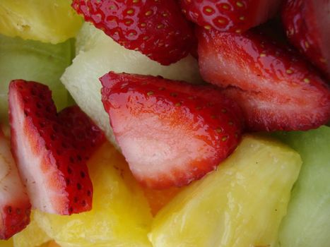 Close up of cut up fruit salad featuring  strewberries, pineapple, and honeydew melon.