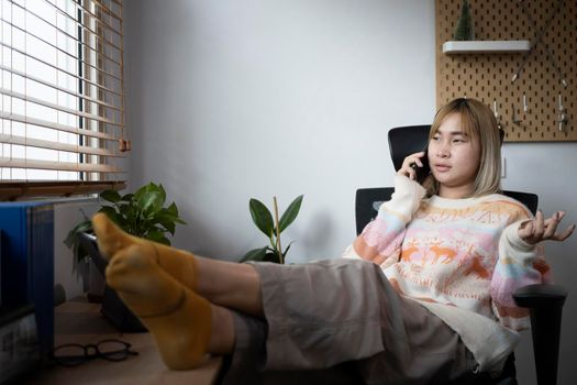Young asian woman sitting on comfortable chair in living room and talking on mobile phone.