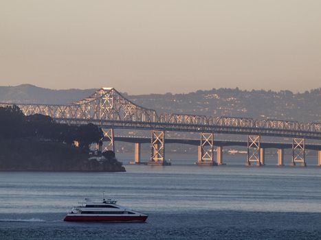 Ferry Boat races by Oakland Bay Bridges at dusk